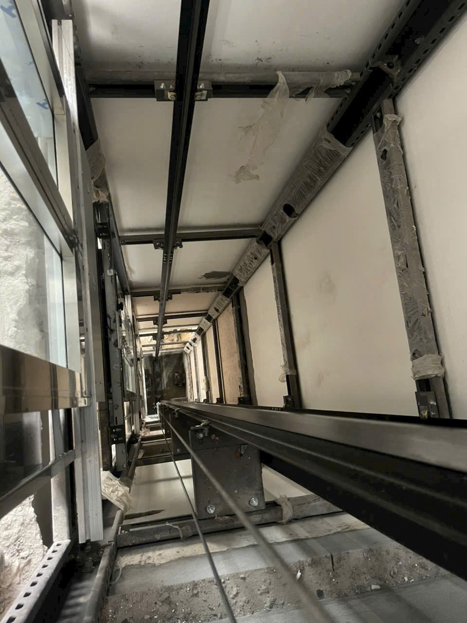 Hố thang máy đang thi công với ray dẫn hướng và hệ thống cáp treo cabin